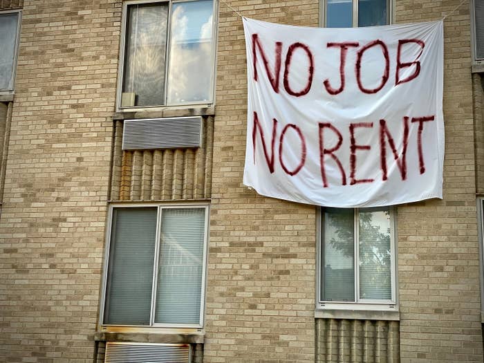 A sheet with "NO JOB NO RENT" painted on it hangs on the outside of an apartment building