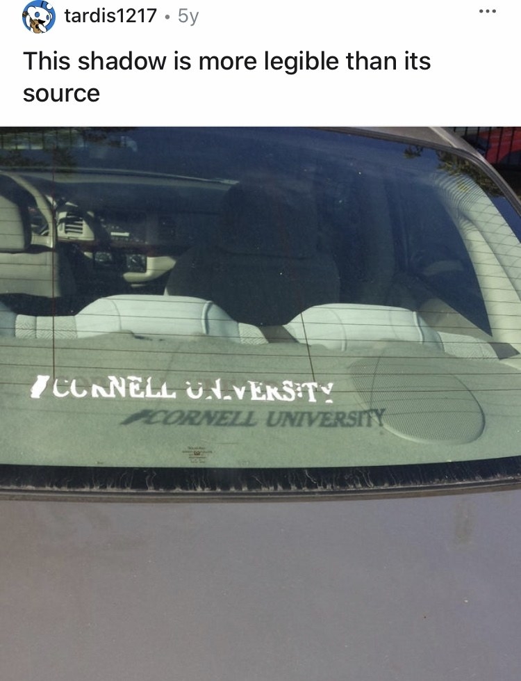 There is a Cornell University decal on the back window of a car that is peeling, but its shadow spells out Cornell perfectly