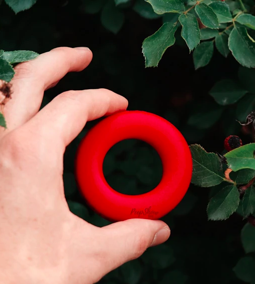 Model holds bendable bright red cock ring in their hands above a flower bush