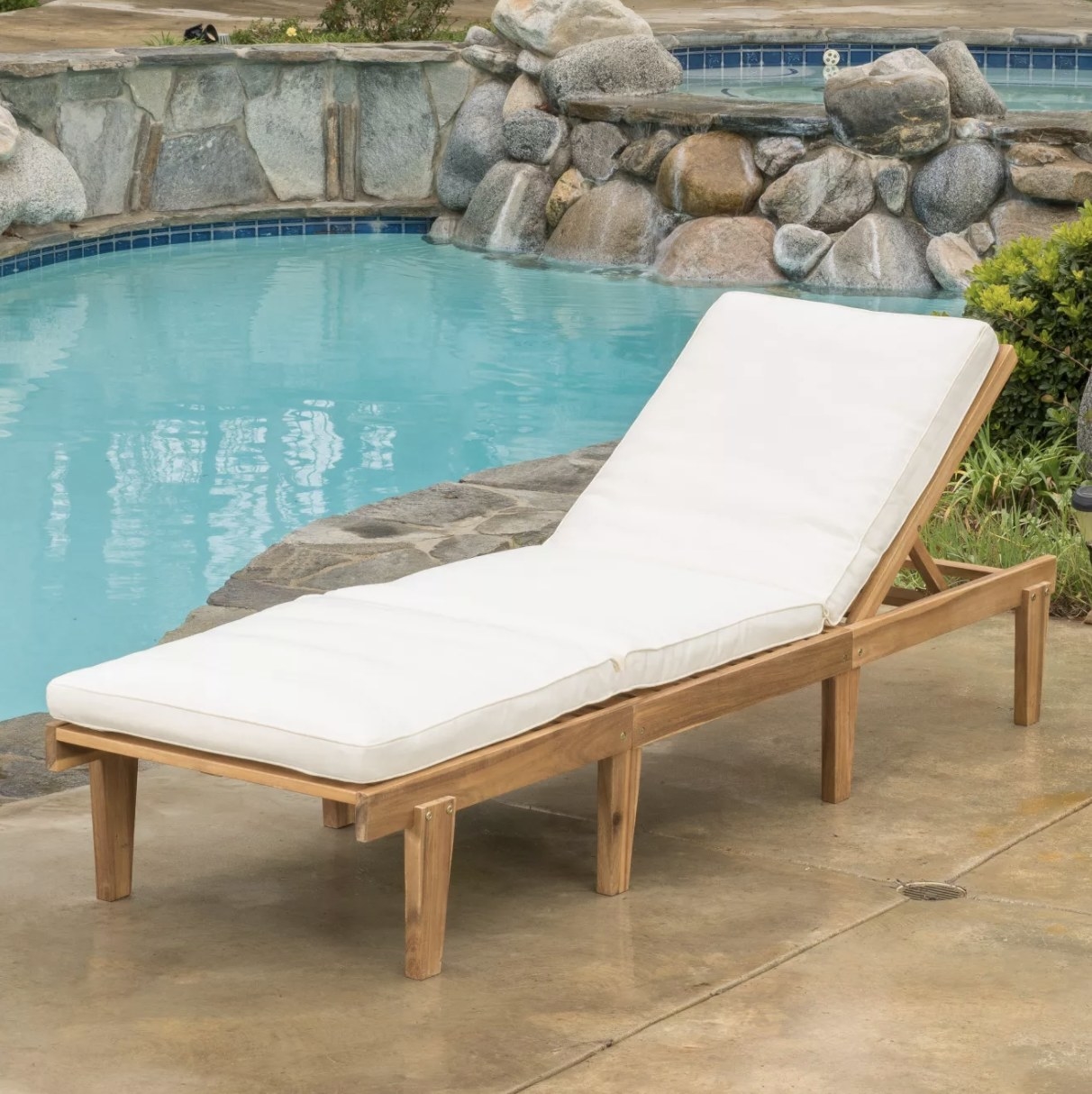 A wooden chaise lounge with a thick white cushion next to a pool