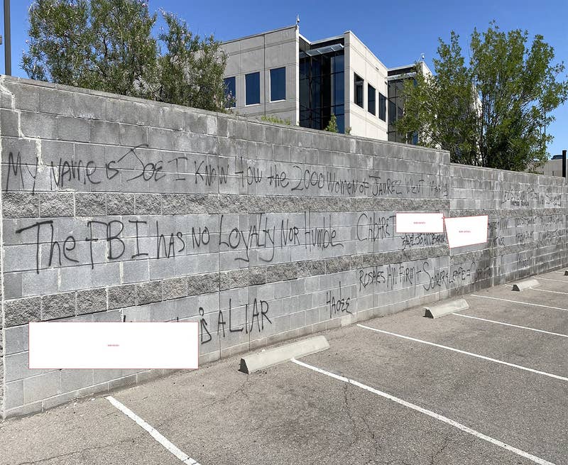 Black graffiti on a wall next to a parking lot reads &quot;The FBI has no loyalty nor humble&quot; among other phrases, while some words are redacted