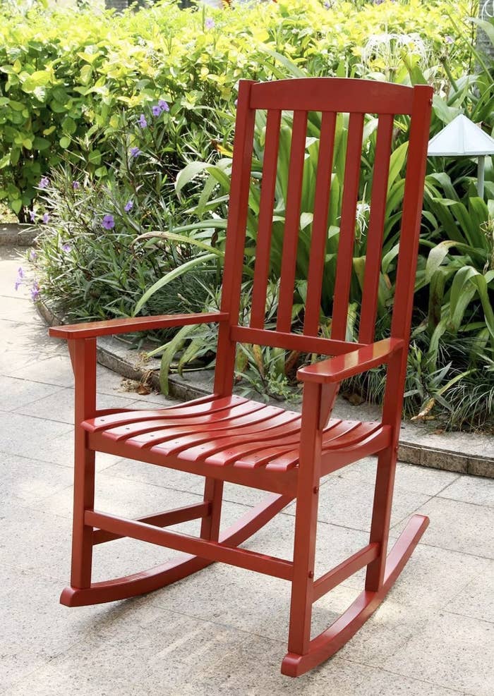 A red rocking chair in front of a garden