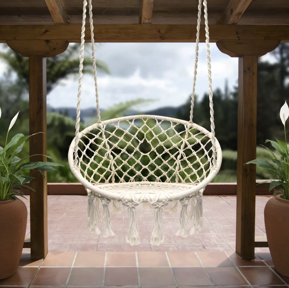 A white, braided chair with tassels hanging from four ropes attached to the ceiling of a patio