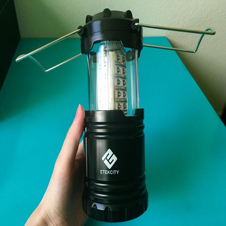 A reviewer's hand holding a fully opened black LED lantern
