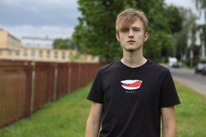 A teen with floppy hair and a trim beard stands outside on a lawn