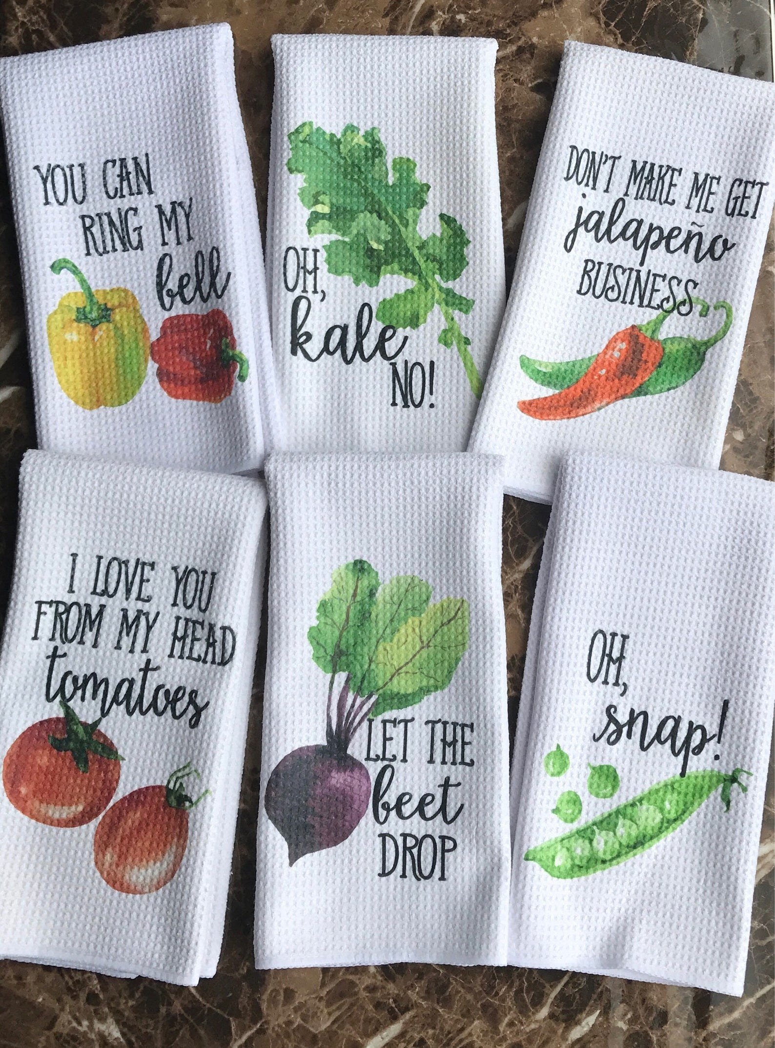 White towels with images of vegetables and puns like &quot;Oh, Snap&quot; and &quot;Let the beet drop&quot; 