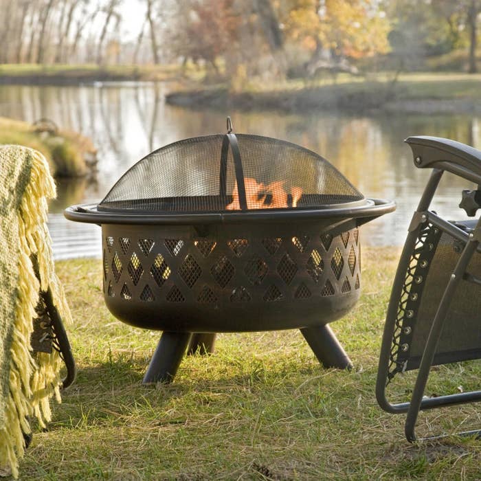 The Coral Coast Rubbed Bronze Crossweave 36 in. Wood Burning Fire Pit burning near a lake