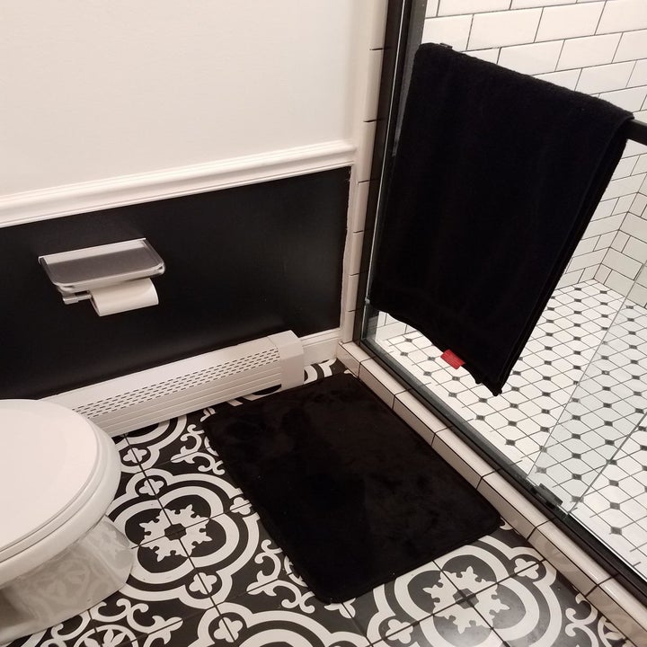 A black rectangular bath mat on a bathroom floor 