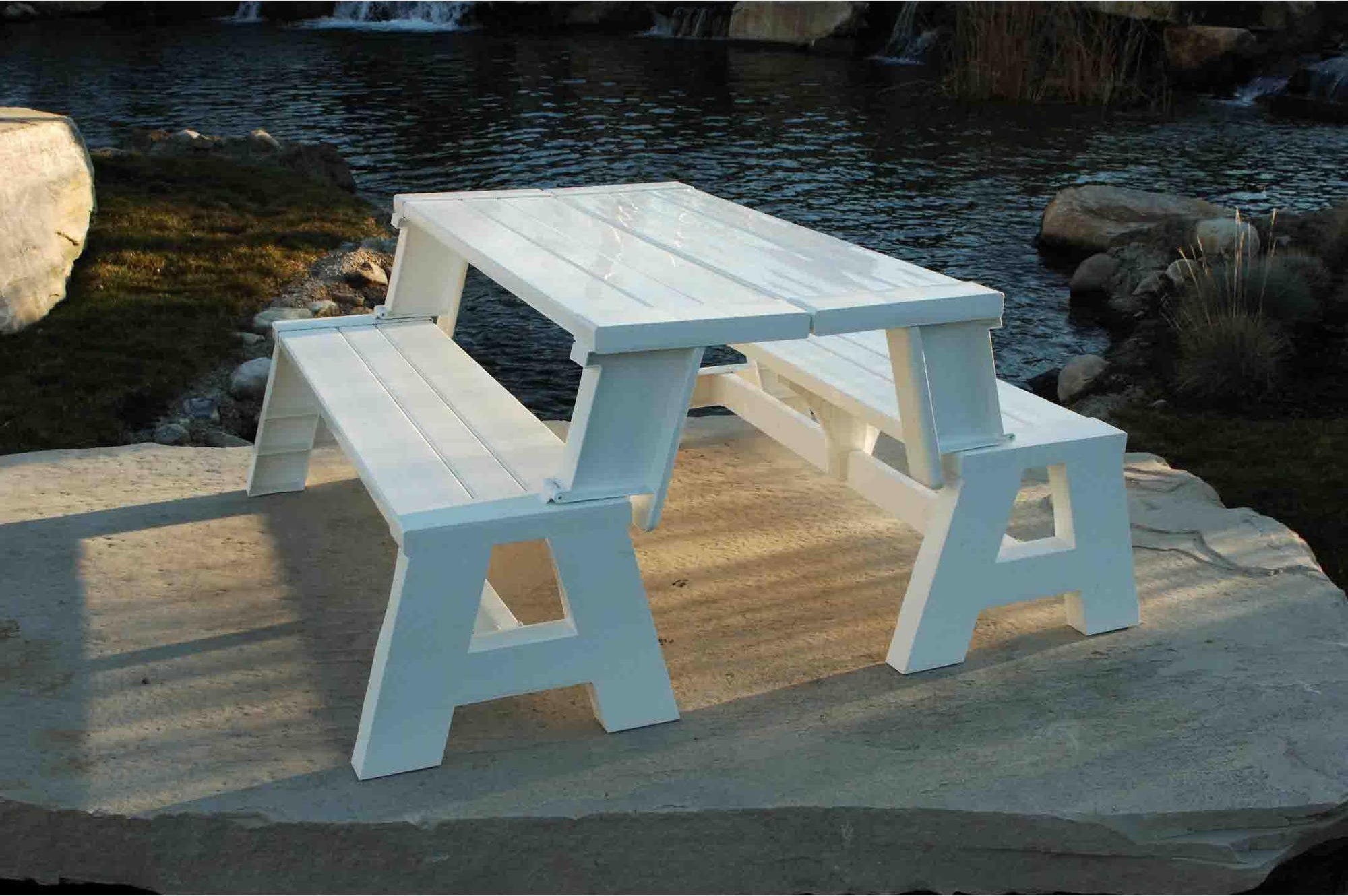 The white Convert-A-Bench Plastic Folding Picnic Table Bench on the edge of a rock by the water