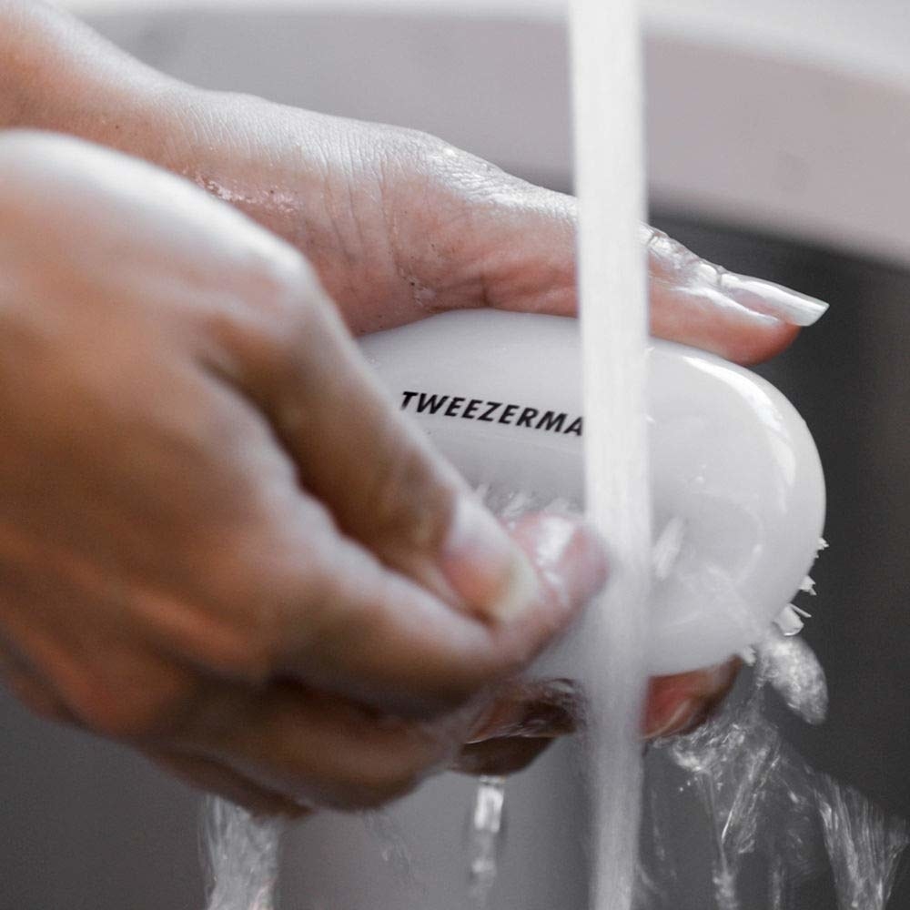 A close up of a person washing their nails with the brush under running water