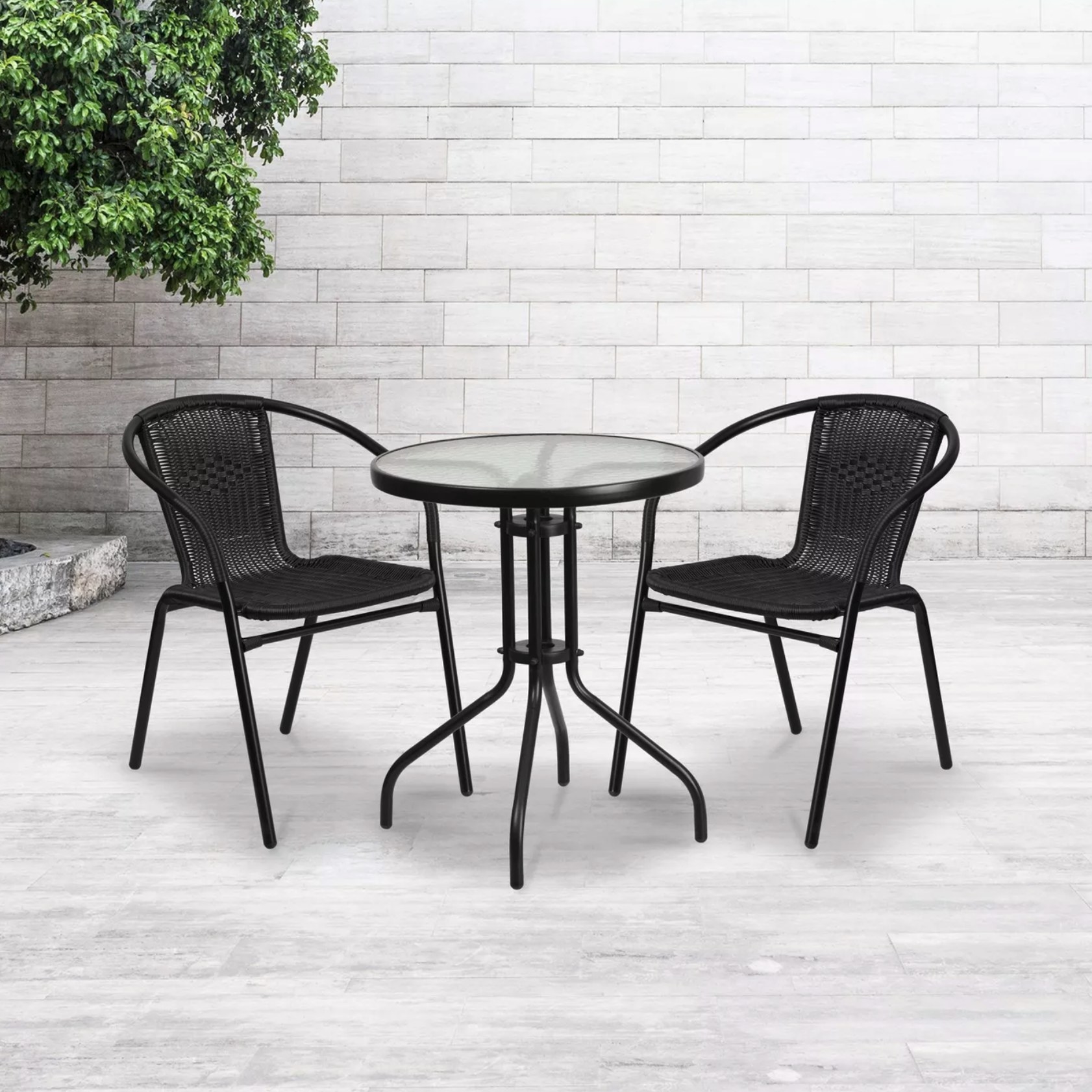 A pair of black rattan armchairs in a tiled outdoor space with a small table
