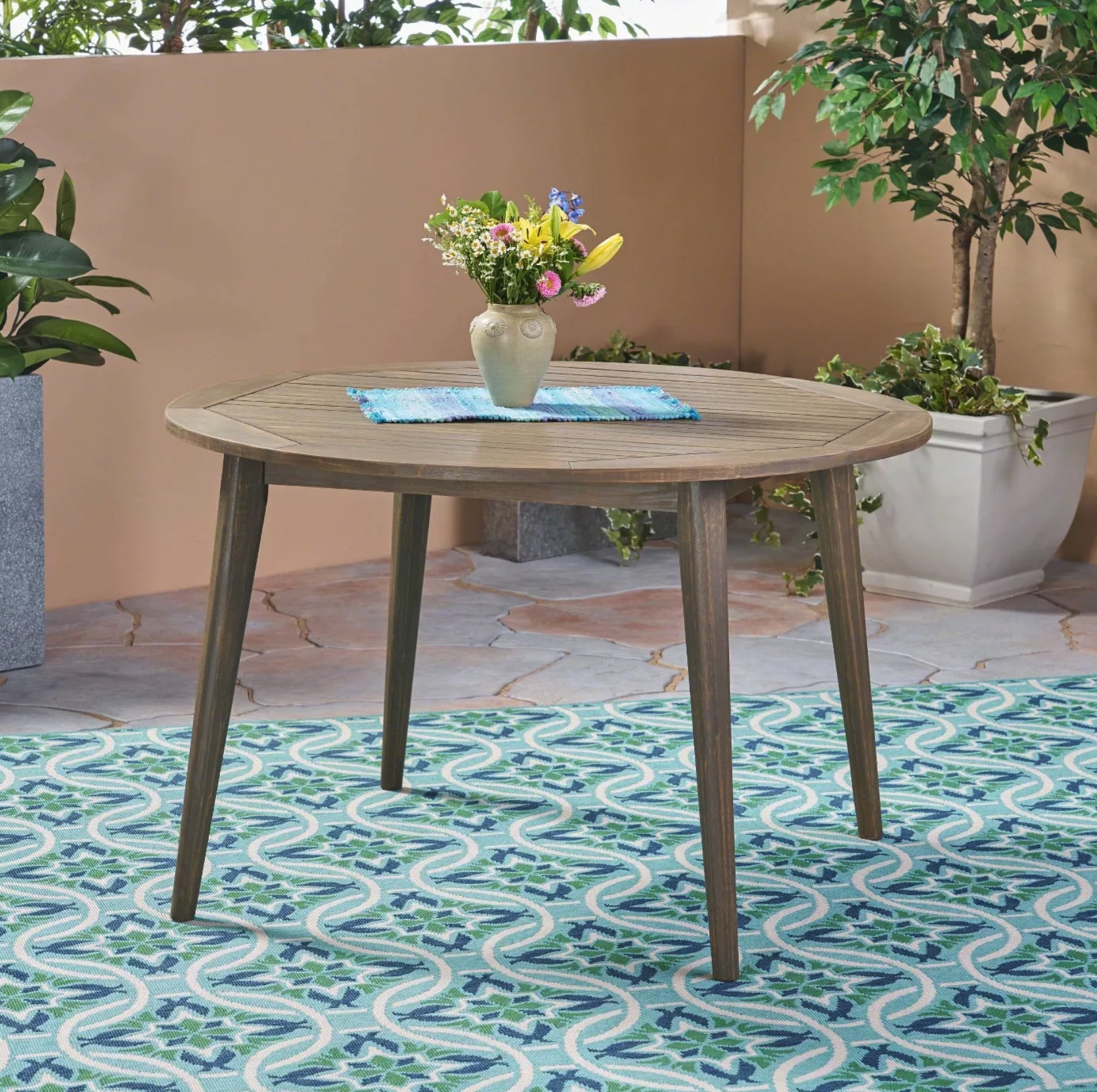 A round, wooden table with an octagonal shape on the top on a colorful rug in a walled patio