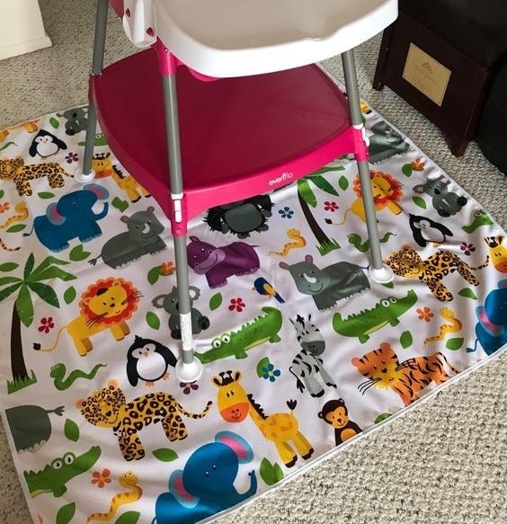 Reviewer's picture of the cartoon safari-themed floor mat under a high chair