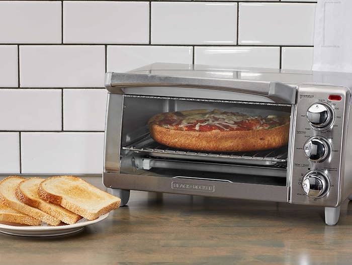 A stainless steel toaster oven with three round knobs and a glass door with a pizza inside