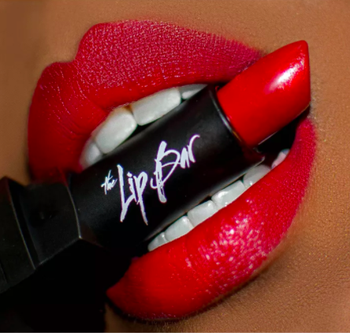 model with dark skin swatched with red The Lip Bar lipstick 