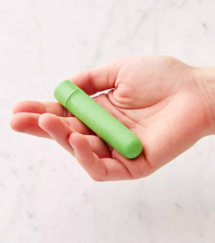 Model holds small green biodegradable bullet vibrator in the palm of their hand