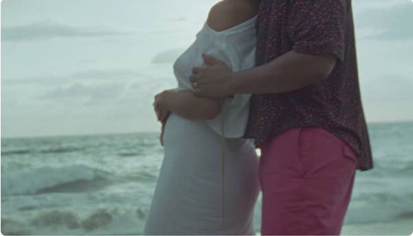 Side view of John and Chrissy holding Chrissy&#x27;s baby bump while overlooking the ocean