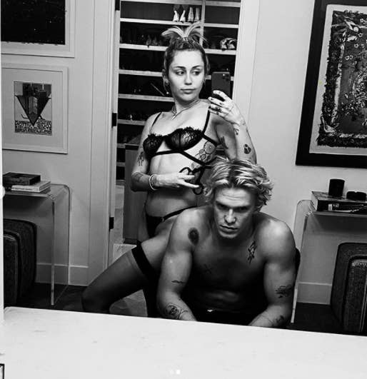 Miley Cyrus wearing lingerie and posing for selfie in front of a mirror with a shirtless Cody Simpson