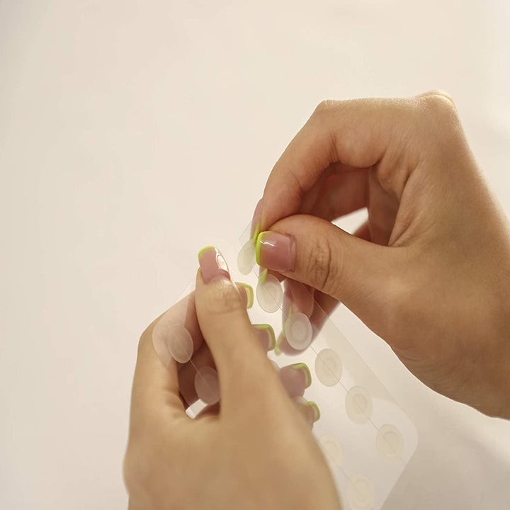 A person removing a pimple patch from its sheet.