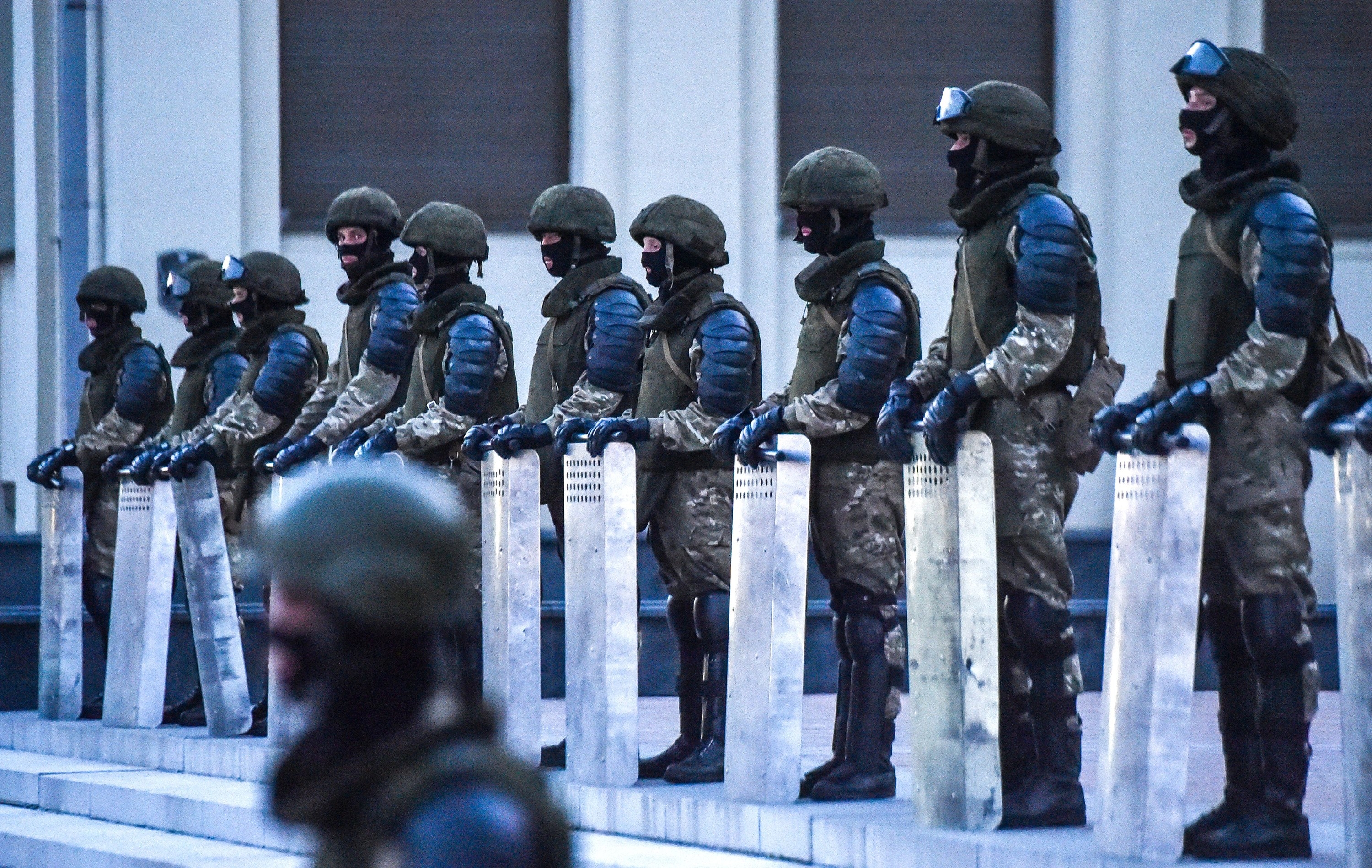 Ten officers in military gear stand in a line holding large shields