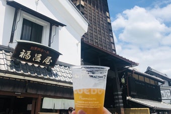 手に持たれたビールカップと川越の時の鐘を背景にした写真。