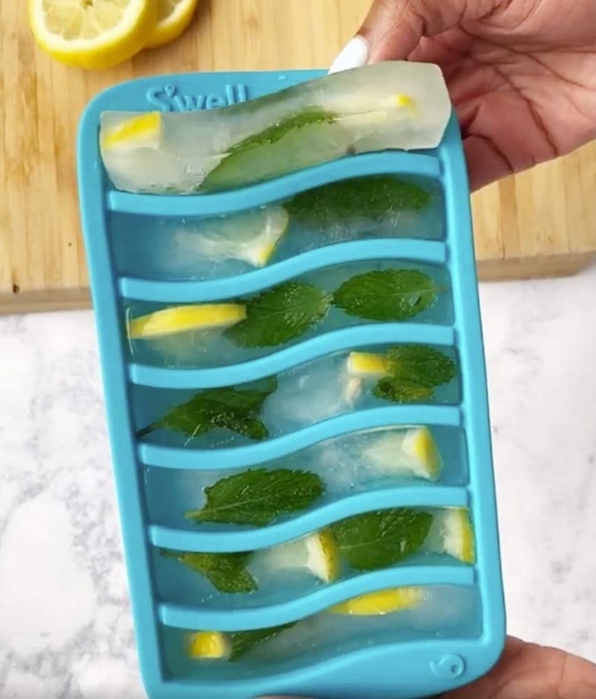 A person holding the ice cube tray filled with lemon-mint ice cubes