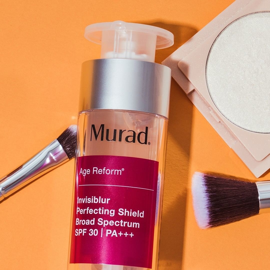 The perfecting shield bottle with two makeup brashes and a blush around it
