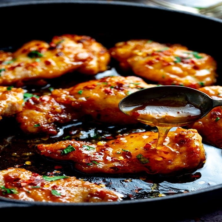A skillet with honey garlic chicken and a spoon, ladling sauce over the pieces of chicken.