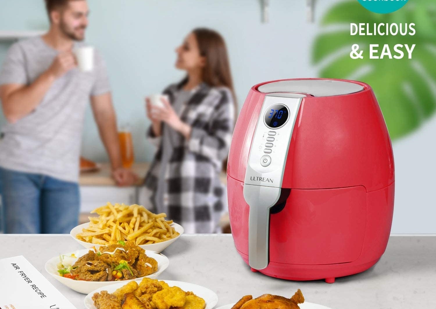 The red air fryer on a counter next to plates of fries, chicken, and other foods