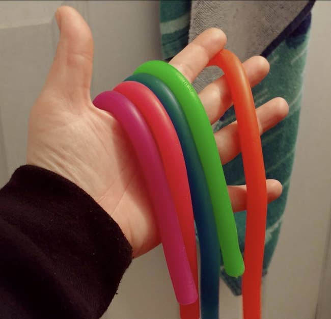 Reviewer holding five long noodle-shaped toys in different colors 