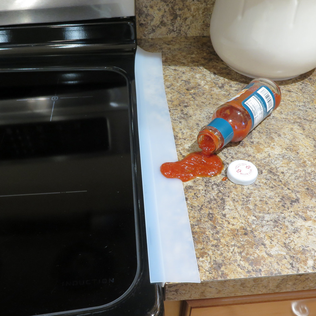 Photo showing Evelots stove counter gap filler preventing a bottle of spilled cocktail sauce from dripping in between the stove and cabinets