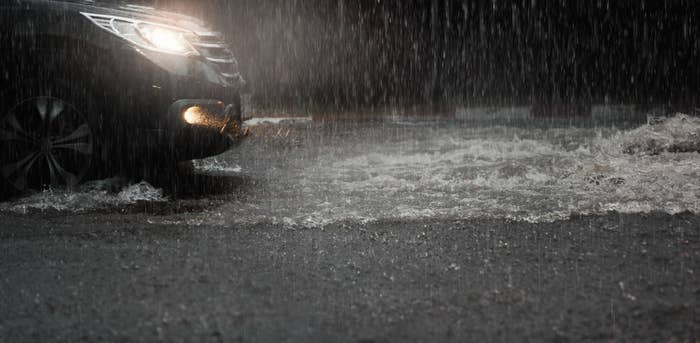 A car with its headlights on and rain pouring down