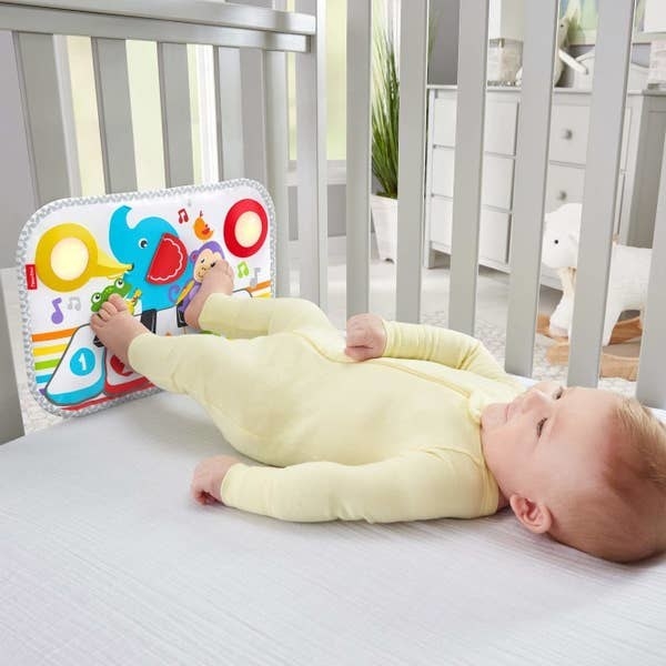 A baby playing with the kick piano in their crib