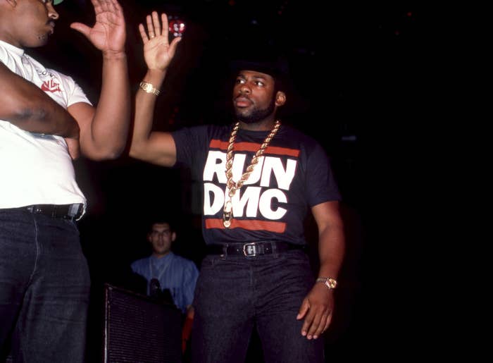 Jam Master Jay wears a thick gold chain and a T-shirt that reads "Run DMC" as he gives another man a high-five