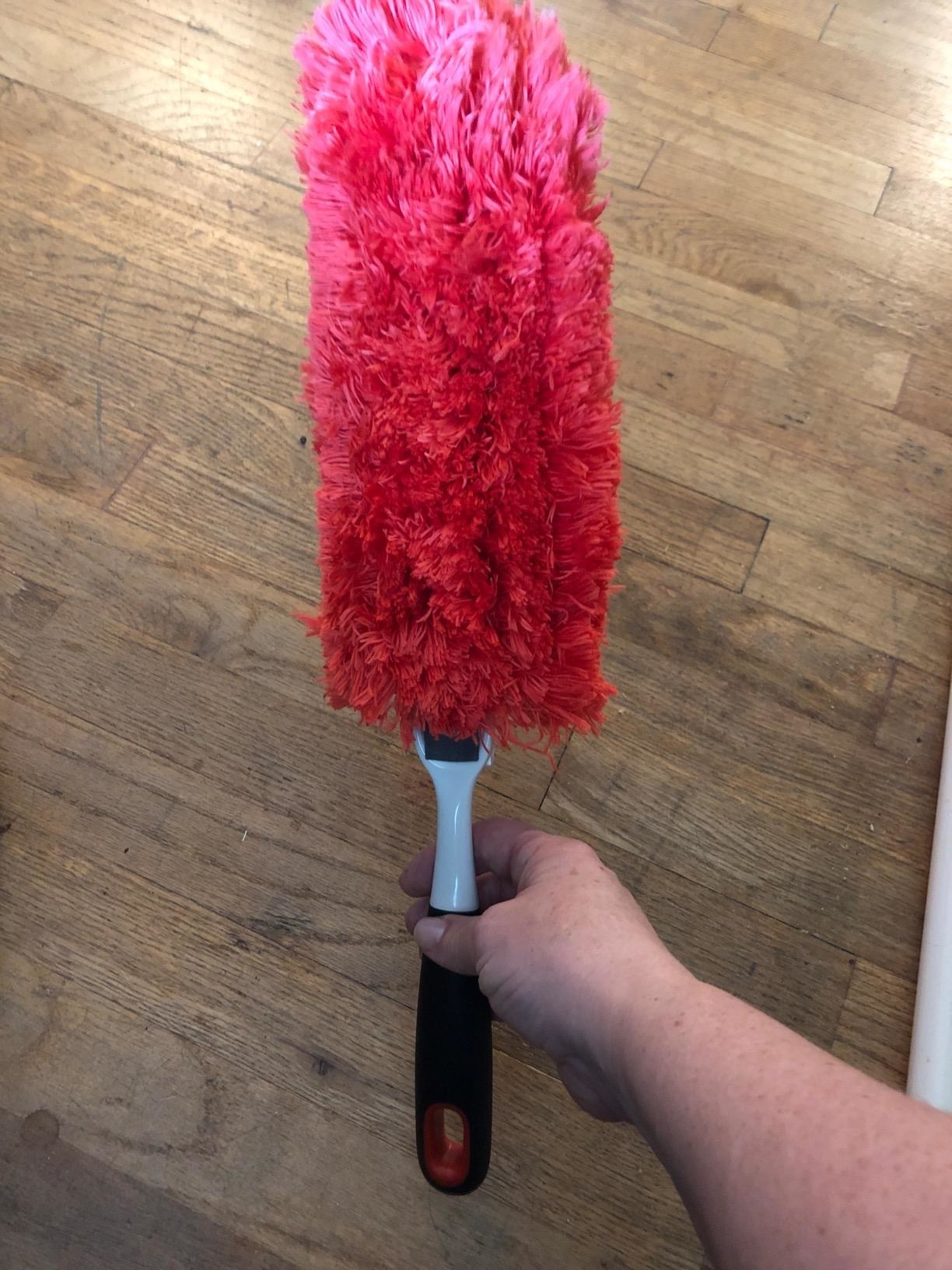 Reviewer holding the duster with a black and white handle and a red microfiber head