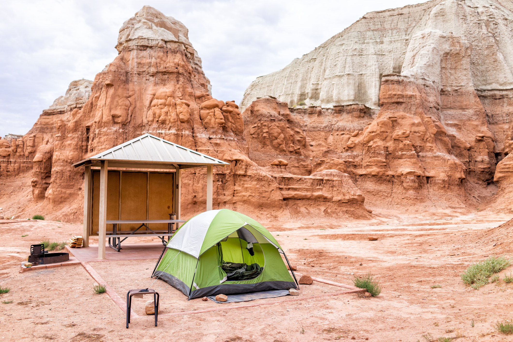 a tent in a marked camp site in Goblin Valley State Park, with white and red layers of sandstone rock formations in the background