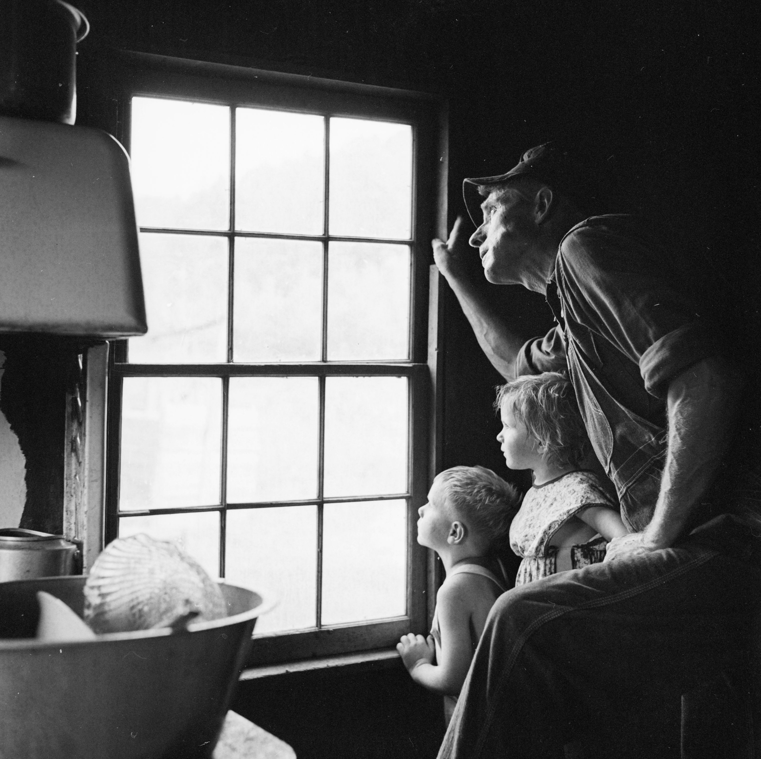 A man looks out a window with two small children 