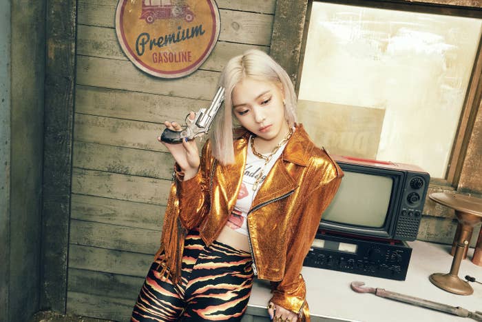 Ryujin looks down despondently while dressed as a cowboy with tiger print shorts and tasseled metallic leather jacket inside a western-themed gas station