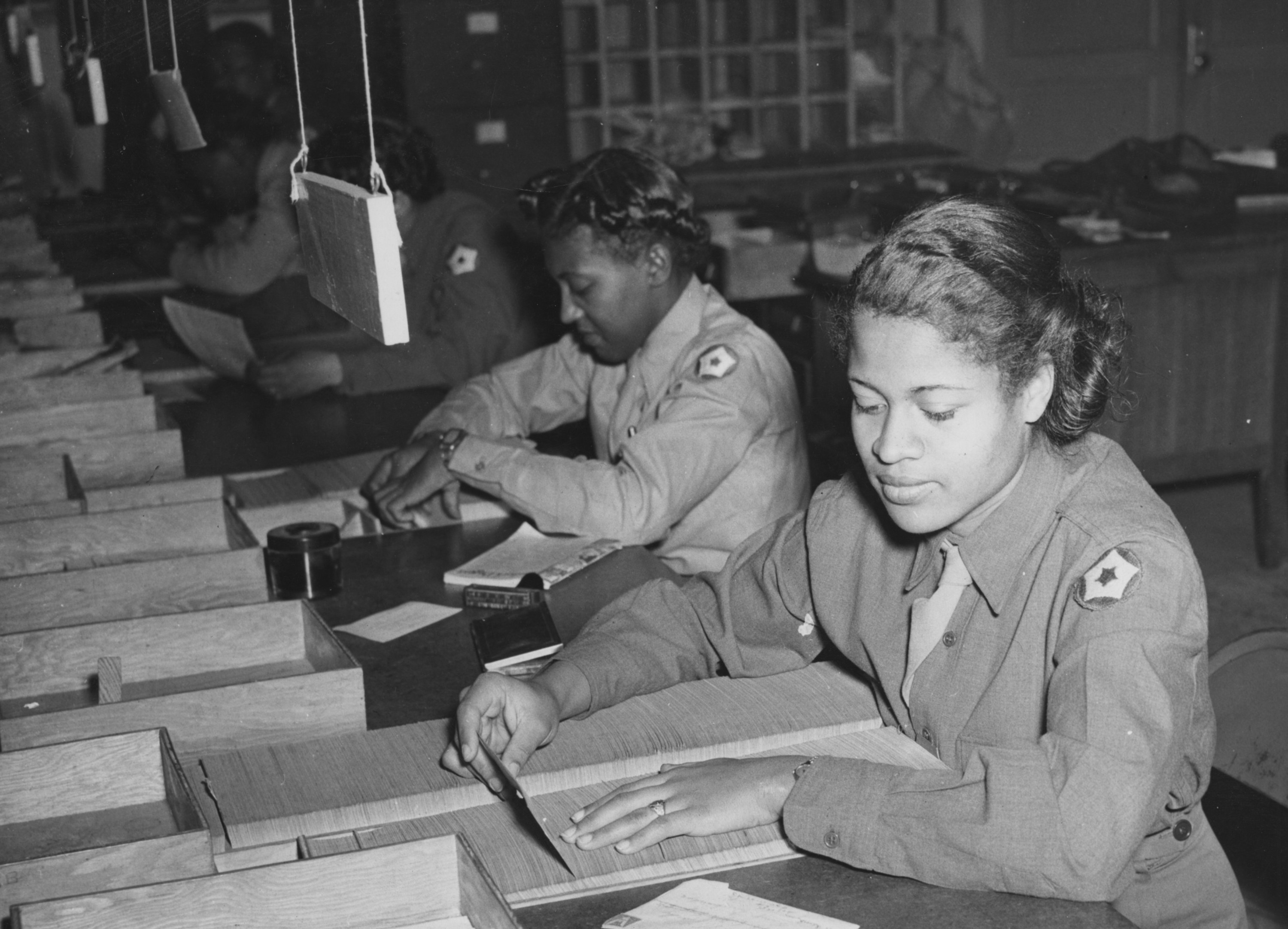 Two black women in military uniforms sort mail