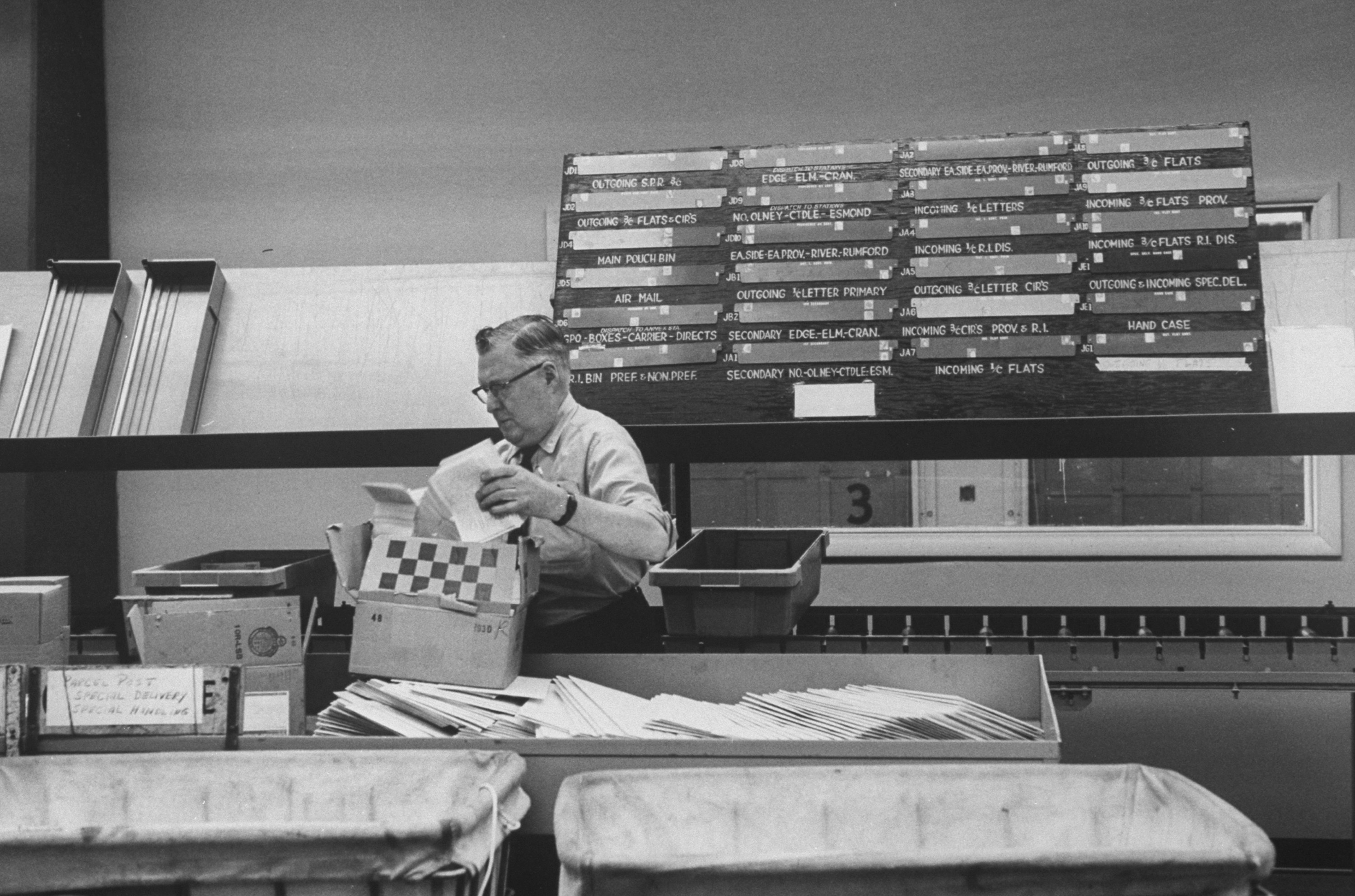 A middle-aged white man in glasses unloads mail onto a conveyer belt