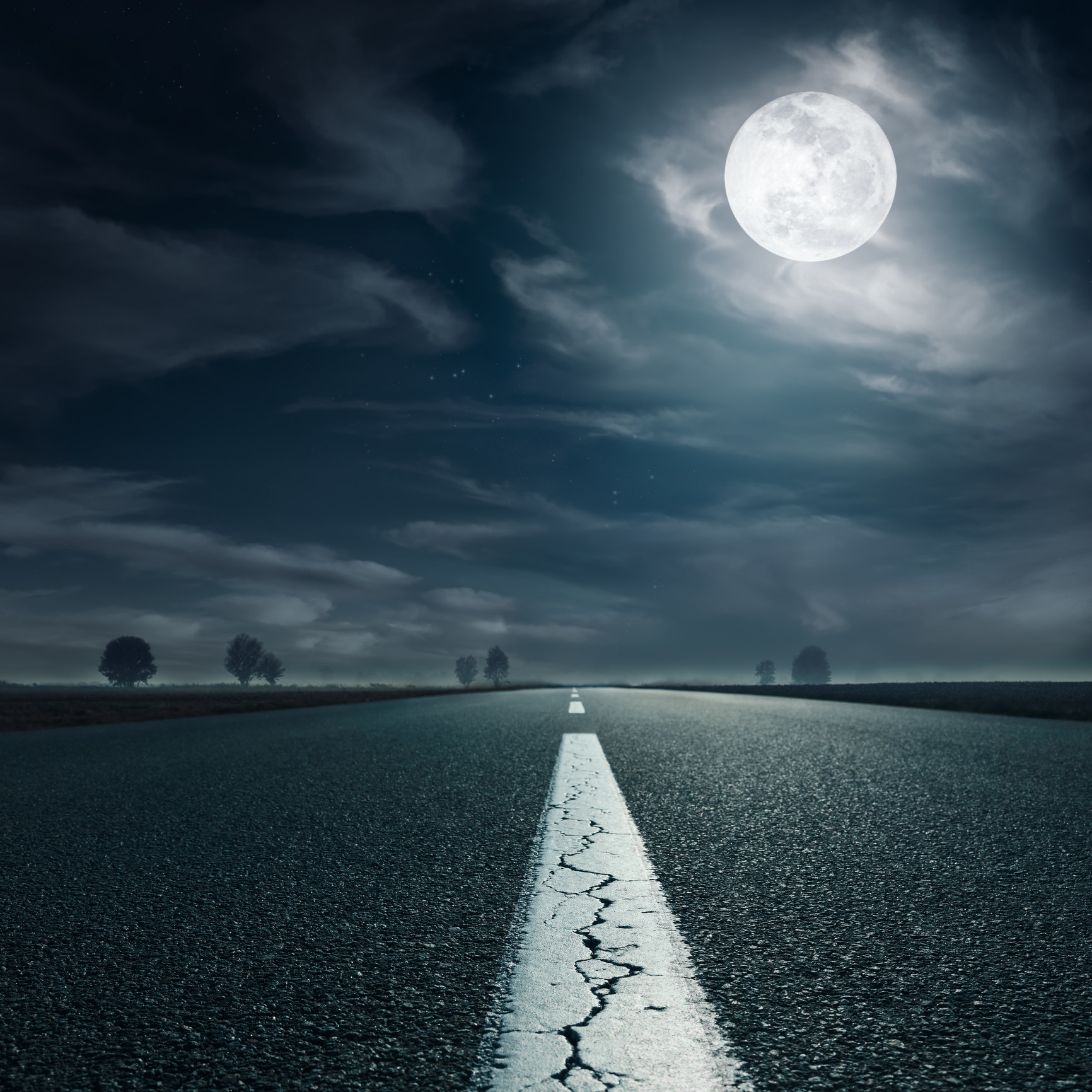 An eerie, empty road at night with a full moon in the sky