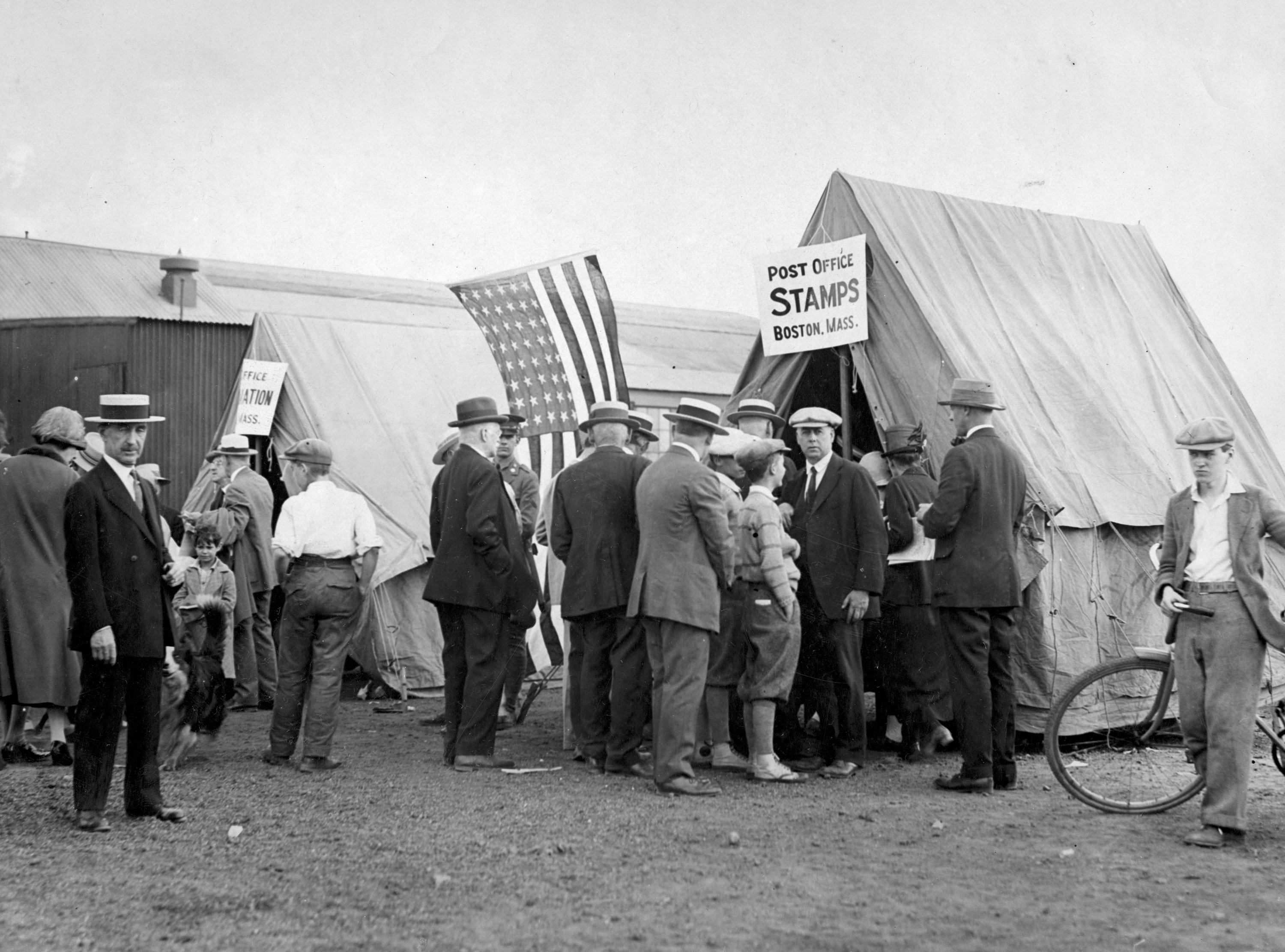 A crowd of people stand in front of a post office tent with a sign that says &quot;stamps&quot;