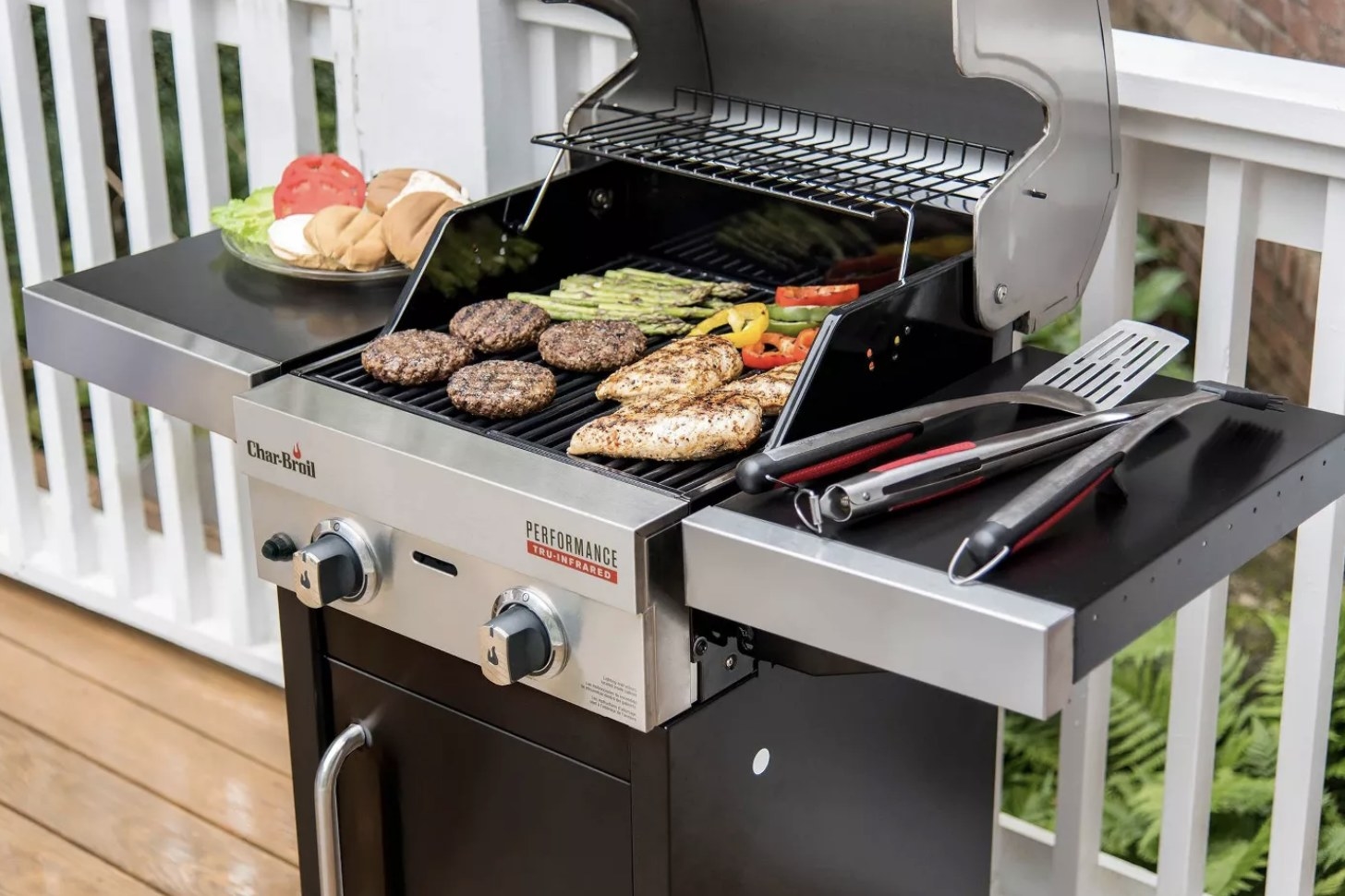 A black-and-aluminum grill with two panels and two burners open to show burgers, chicken, and veggies cooking