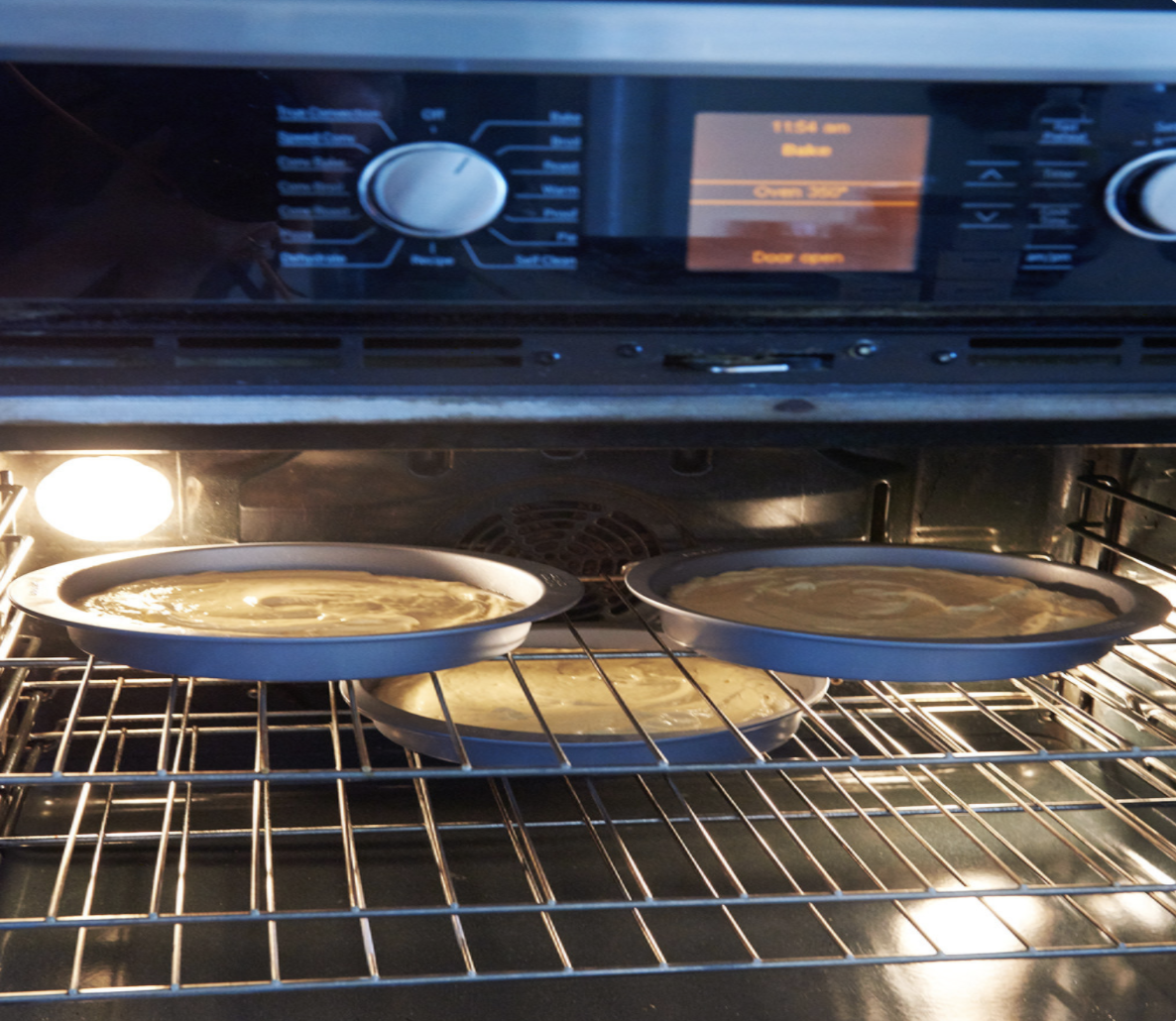 An oven with its door open, while three cakes are baking inside