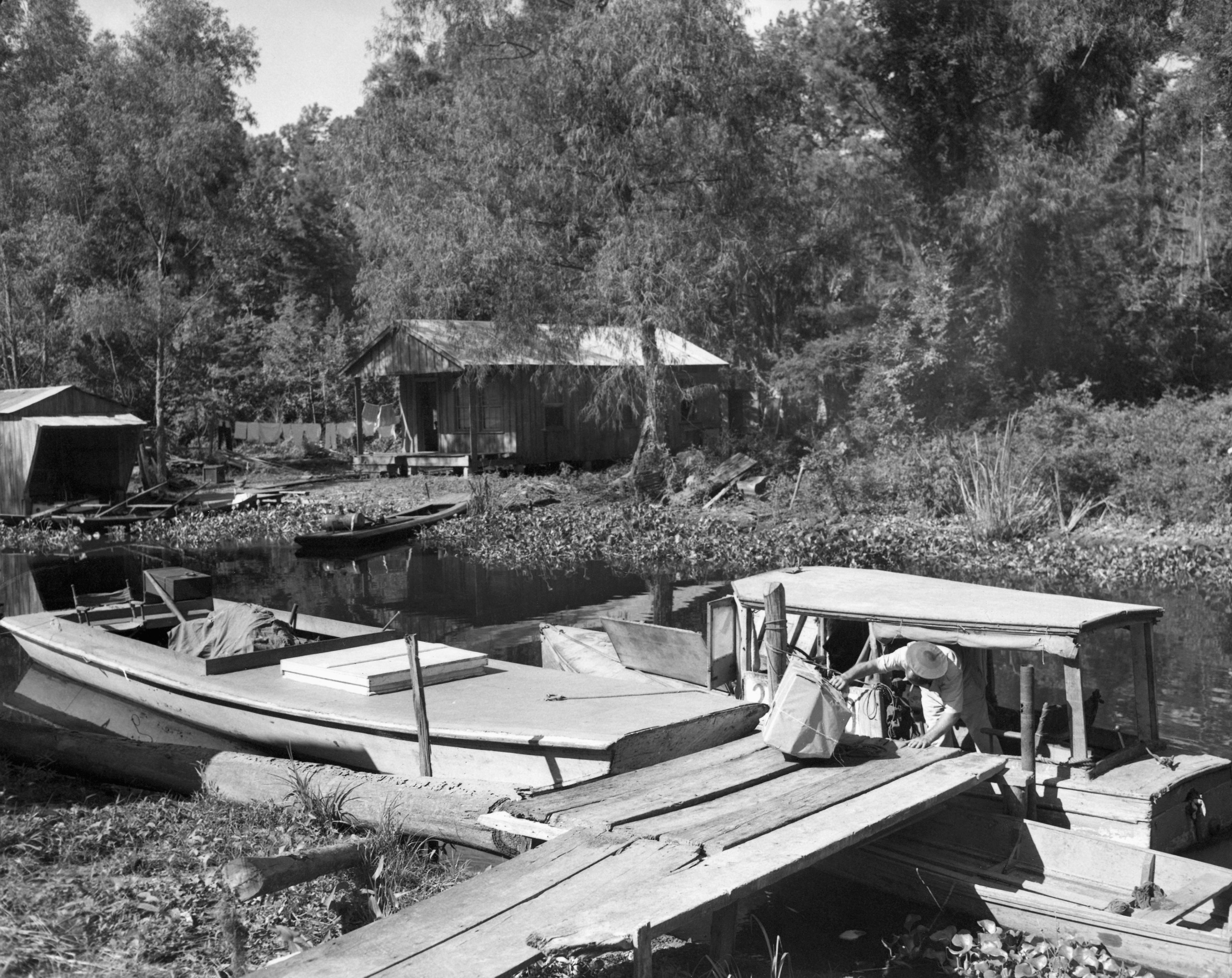 A man gets on a wood boat with a sack of mail in a bayou