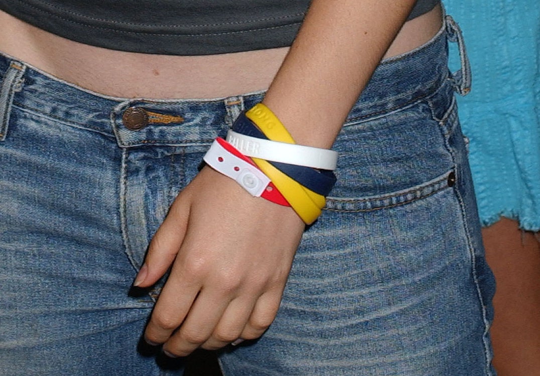An arm with various cause bracelets against a pair of low-rise jeans.