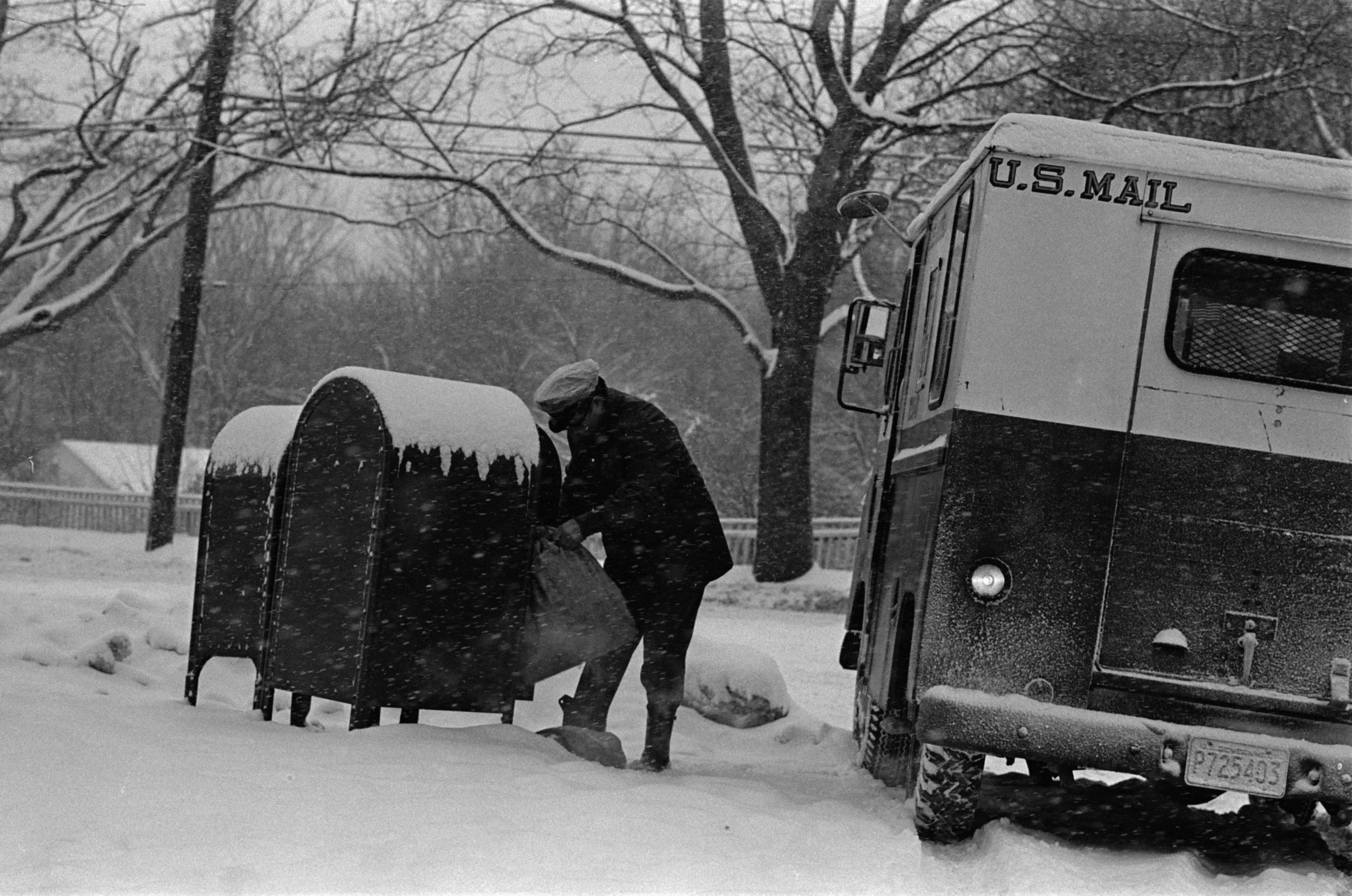 A man unloads mail from mailboxes covered by snow