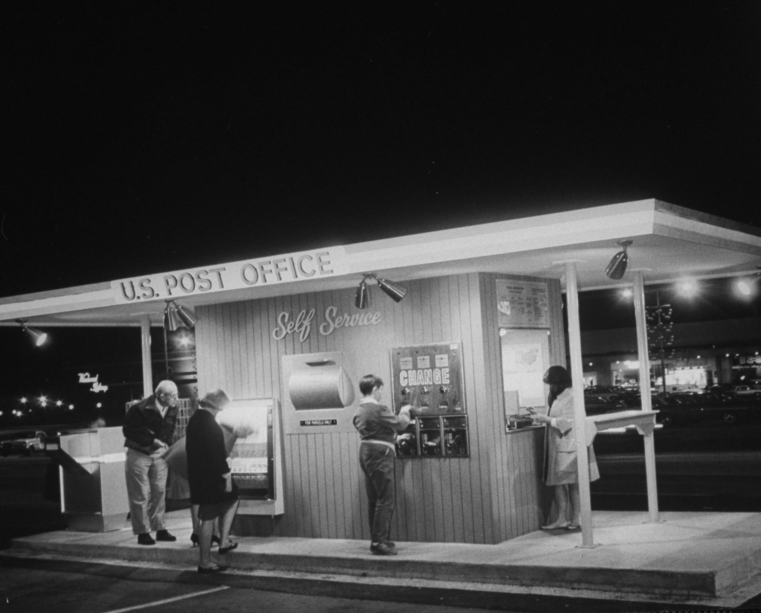 Four people at a mail kiosk that offers change and stamps