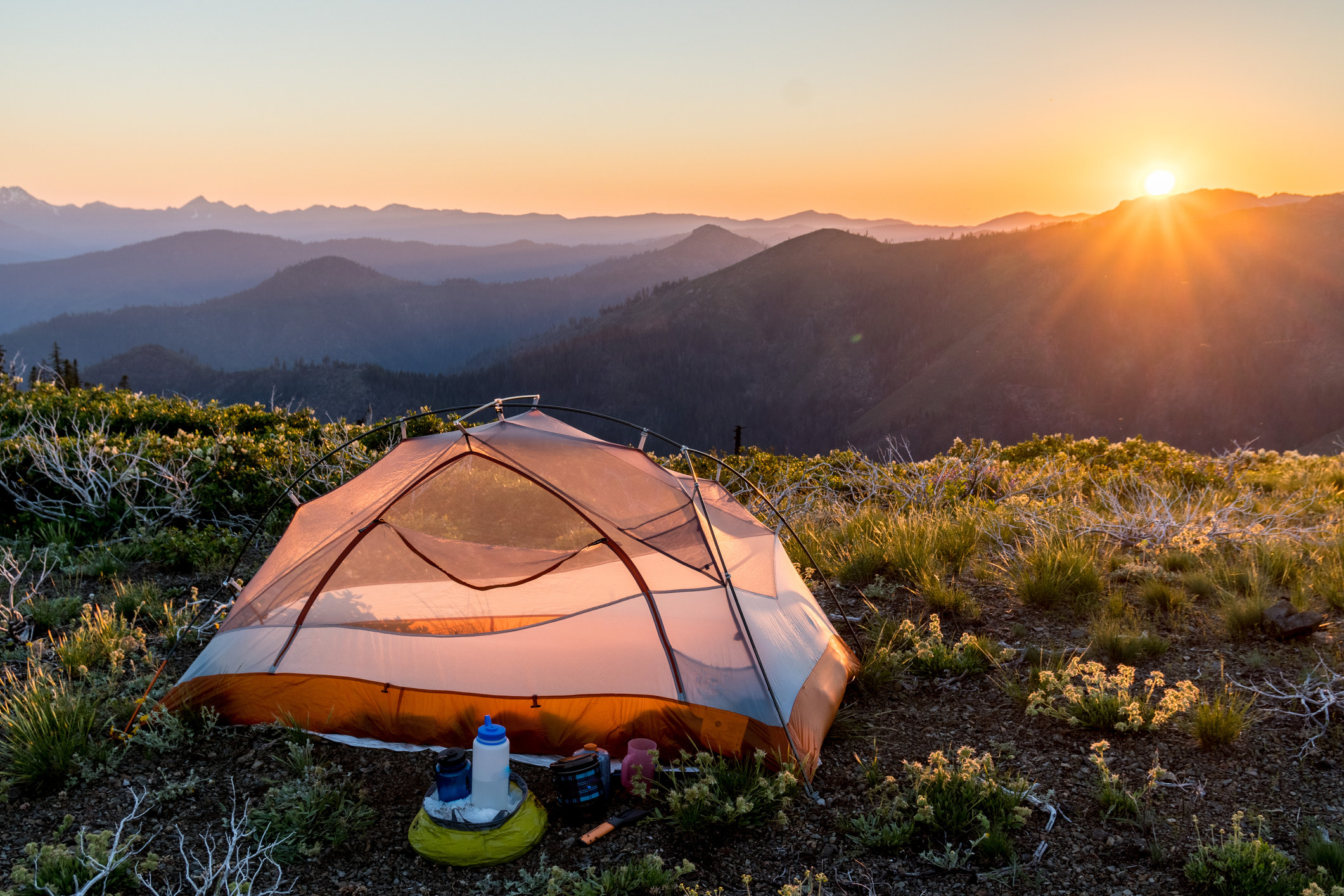 a remote tent on a flat mountain top with the sunset in the background