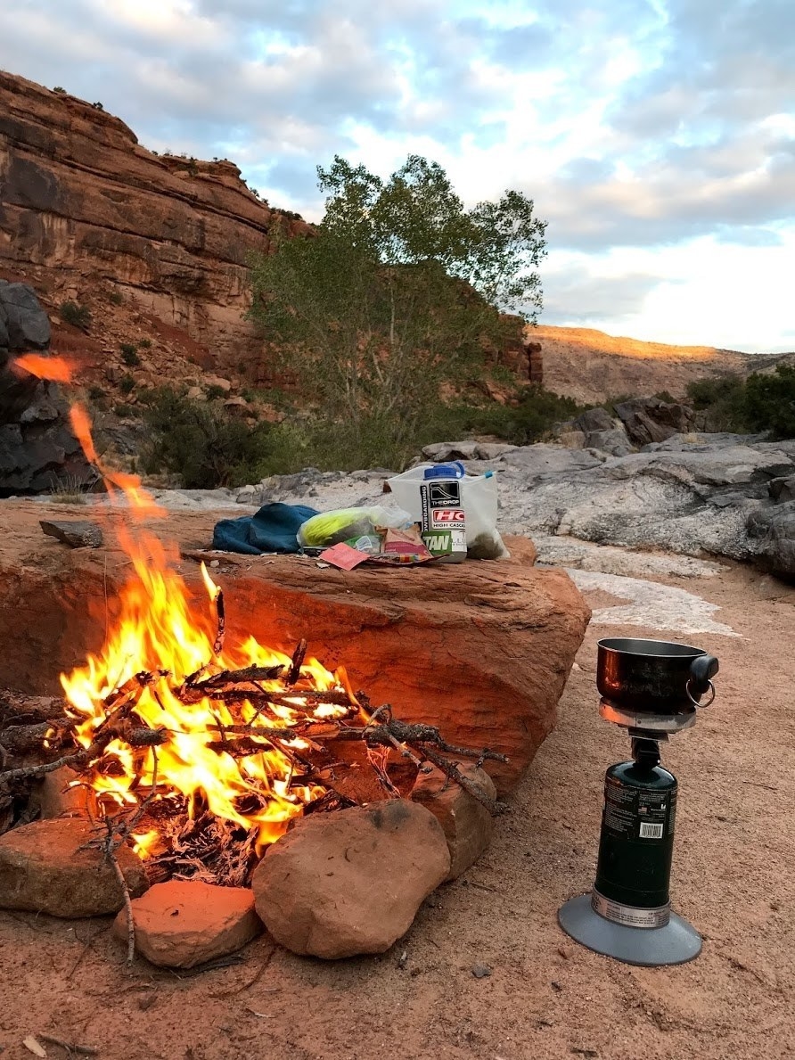 roaring campfire surrounded by rocks and camping gear